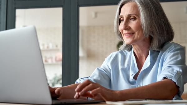 Eine Frau mit schulterlangen grauen Haaren sitzt vor einem Laptop.